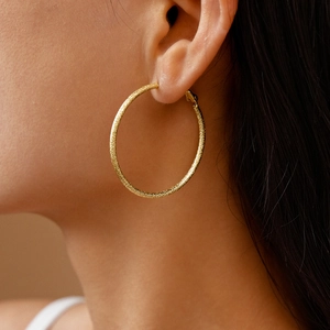 Detail of a large gold textured hoop earring shown on a model for stylish daily wear