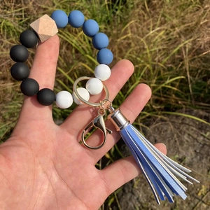 Detail of beaded keychain bracelet with blue silicone beads and fringe tassel held by hand