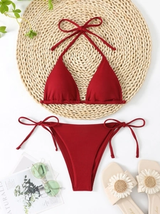 Flat lay of wine red ribbed bikini set on woven mat with summer vacation accessories