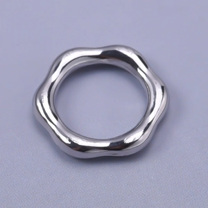 Close-up of a silver irregular wave-shaped stainless steel pendant on a grey surface