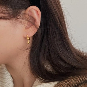 Close-up of minimalist golden beaded stud earring with small round sphere pendant on model