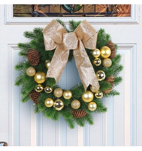 Close-up of Christmas wreath with golden glitter bow and pine cones on a white door