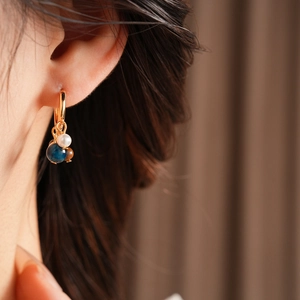 Detail of vintage gold hoop earring with tiger eye bead, blue stone, and white pearl drop