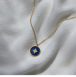 Close-up of blue enamel star compass pendant necklace on white draped fabric