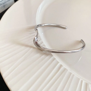 Detailed top view of a polished silver wave-shaped open cuff on a white textured tray
