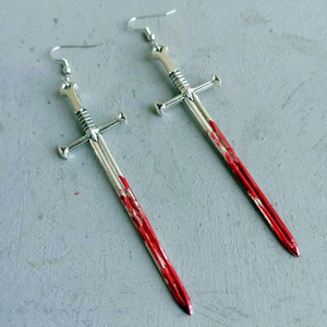 Detailed macro view of gothic silver sword earrings with realistic red blood splatters