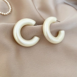 Detailed view of pearl-like C-shaped acrylic earrings on a golden silk fabric background
