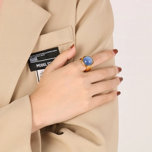 Close-up of a wide 18K gold-plated ring featuring a round blue gemstone on a model