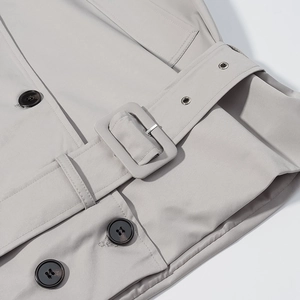 Detail of light gray trench coat featuring a matching fabric belt buckle and black buttons