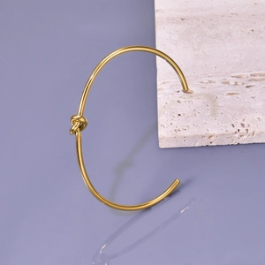 Macro detail of high-polish gold knot cuff bracelet on a minimalist lavender surface