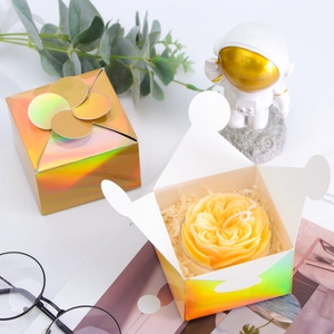 Close-up of holographic gold gift box with handmade rose shaped scented candle and paper filler