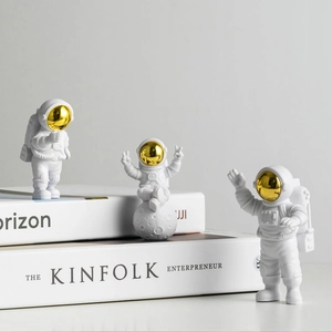 Three white astronaut figurines in different poses placed on books with gold visors