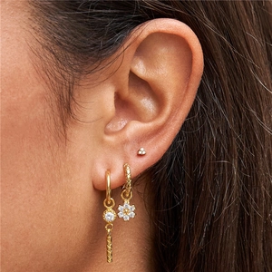 Close-up of gold flower earrings set with zircon studs and drop pendants on ear