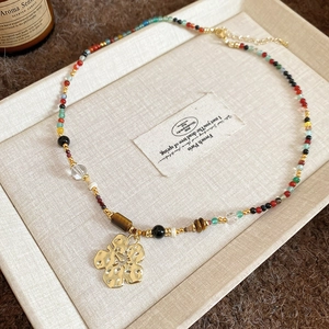 Detail of beaded necklace with gold hammered flower pendant and colorful resin crystals