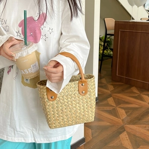 Detailed view of hand-woven straw tote bag with brown leather handles and metal rivets