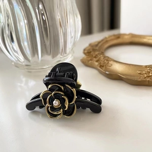 Detailed close-up of small black camellia hair claw clip with pearl accents and gold trim