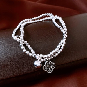 Close-up of double-layer beaded silver bracelet with flower charm and bell pendant