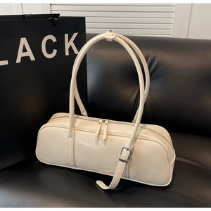 Macro shot of a cream white baguette bag with glossy finish and silver buckles on a sofa