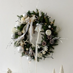 Couronne de Noël élégante blanc et argent avec cônes et LED sur mur blanc