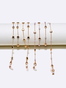 Chaînes de lunettes dorées avec étoiles et perles blanches sur un support minimaliste