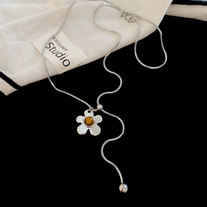 Detail of silver snake chain necklace featuring a floral pendant with amber bead center