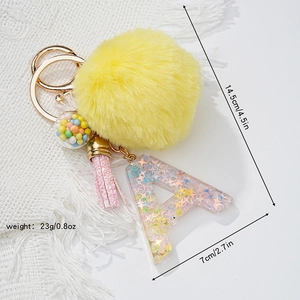 Detail of yellow fluffy ball keychain with pink tassel and colorful resin letter A
