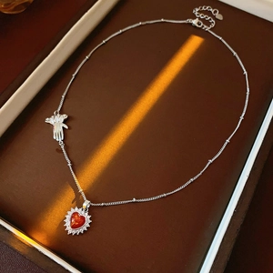 Detailed close-up of a silver heart necklace with red zircon and glove charm in a jewelry box