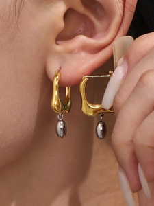 Macro shot of gold irregular hoop earring with silver oval pendant worn on ear