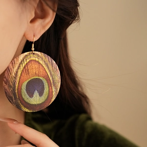 Close-up of bohemian round peacock feather earrings with golden hooks on a model