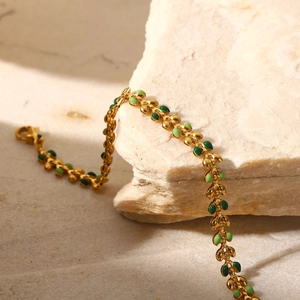 Detailed shot of gold leaf bracelet with green enamel on a beige stone surface