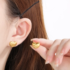 Gros plan sur des boucles d'oreilles cœur en or mat avec texture brossée et design 3D