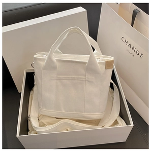 Detailed view of a white canvas tote bag with shoulder strap inside an elegant gift box