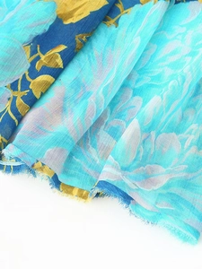 Close-up of sky blue floral chiffon fabric with golden leaf pattern and frayed edge detail