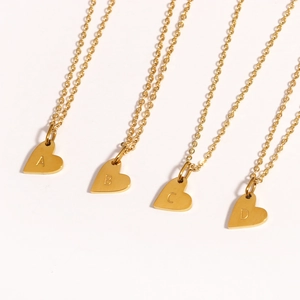 Détail de quatre pendentifs coeur dorés avec les lettres A, B, C et D gravées sur chaînes