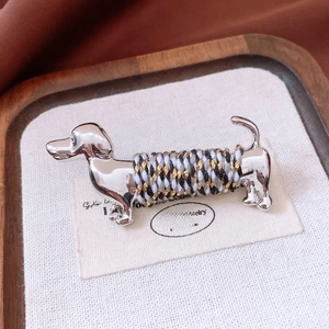 Macro shot of silver dachshund brooch with tricolor woven rope on textured fabric
