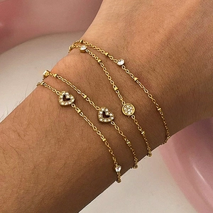 Dettaglio di un bracciale multistrato in acciaio dorato con ciondoli a cuore sul polso