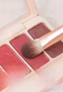 Dettaglio di un pennello da trucco che preleva polvere da una palette di ombretti glitter