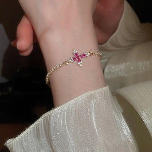Nahaufnahme eines eleganten Gold-Armbands mit Kreuz, rotem Zirkon und Diamanten