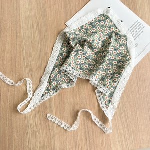 Detail of green floral bandana with lace trim and ties on light wooden surface