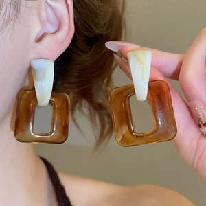 Close-up of geometric resin drop earrings featuring amber brown and cream marble textures