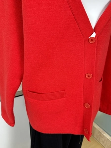 Detail of red oversized knit cardigan showing V-neckline, buttons and side pocket texture