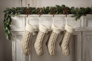 Set of four knitted Christmas stockings hanging on a white fireplace with greenery