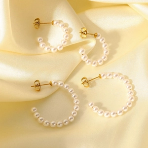 Detailed view of two pairs of C-shaped pearl earrings with gold pins on silk fabric