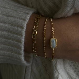 Detailed view of triple gold-plated bracelets with an oval opal pendant on a white sweater