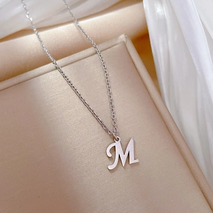 Minimalist silver letter M pendant necklace on elegant champagne satin fabric background