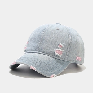 Détail de la broderie rose 1999 et des trous déchirés sur la casquette en denim bleu clair