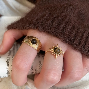 Close-up of gold rings with tiger eye stones worn by a model in a brown knit sweater