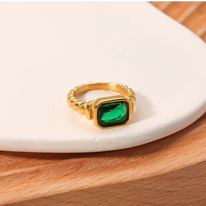 Detail of emerald green rectangular ring with twisted gold band on white tray