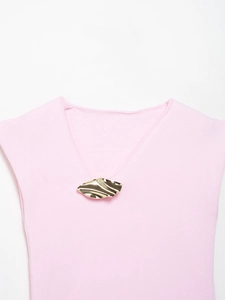 Close-up of a golden abstract wave leaf brooch on a pink V-neck knit top