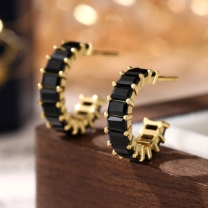 Macro shot of gold C-shaped earrings with square black zircon inlay on wood